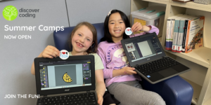 Two young girls, smiling brightly, pose with laptops in hand after a Discover Coding class at Earl Buxton Elementary School.